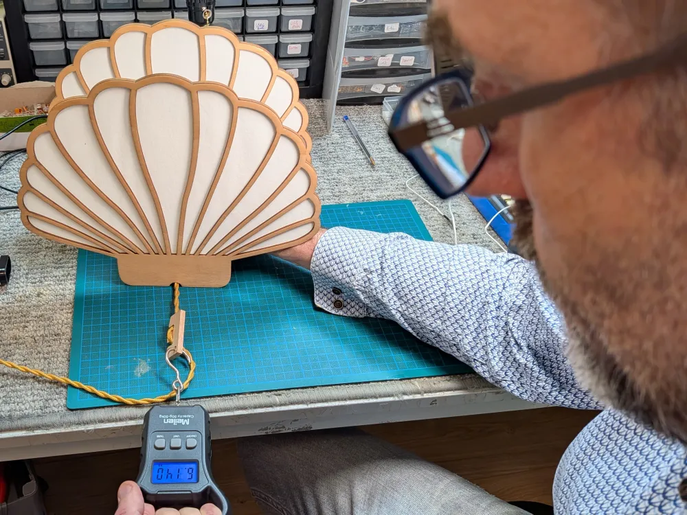 Essai de traction sur une suspension en bois en forme de coquillage : un dynamomètre tire sur le câble de suspension.