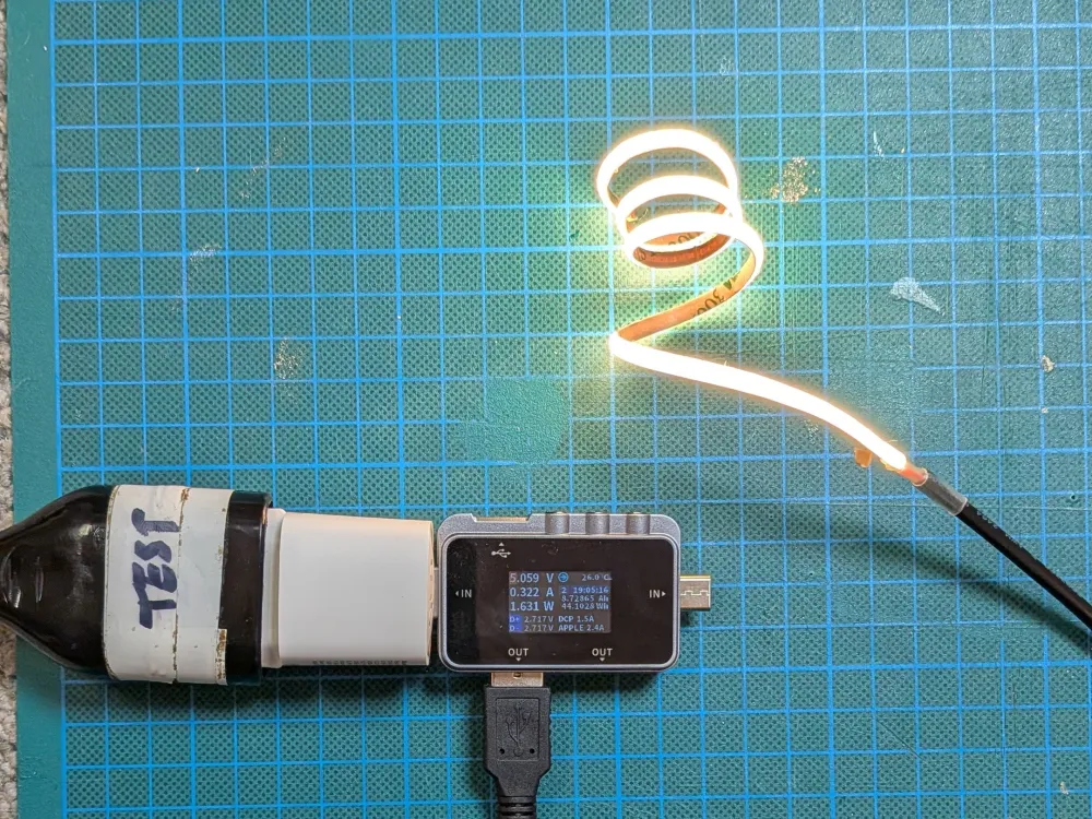 Module LED souple allumé sur un tapis de découpe, relié à un wattmètre qui mesure la tension, le courant et la puissance absorbée.