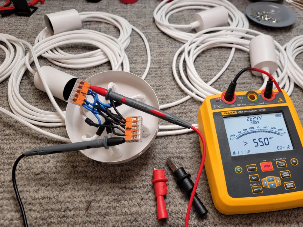 Mesure d'isolement sur le boîtier de connexion d'un luminaire : deux pointes de touche reliées à un contrôleur d'isolement.