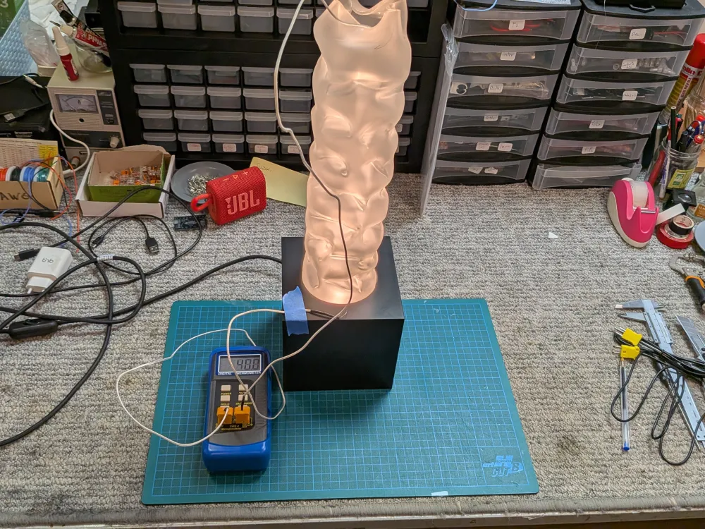 Luminaire sculpté allumé sur l'établi, un thermocouple fixé sur son socle et relié à un thermomètre numérique.